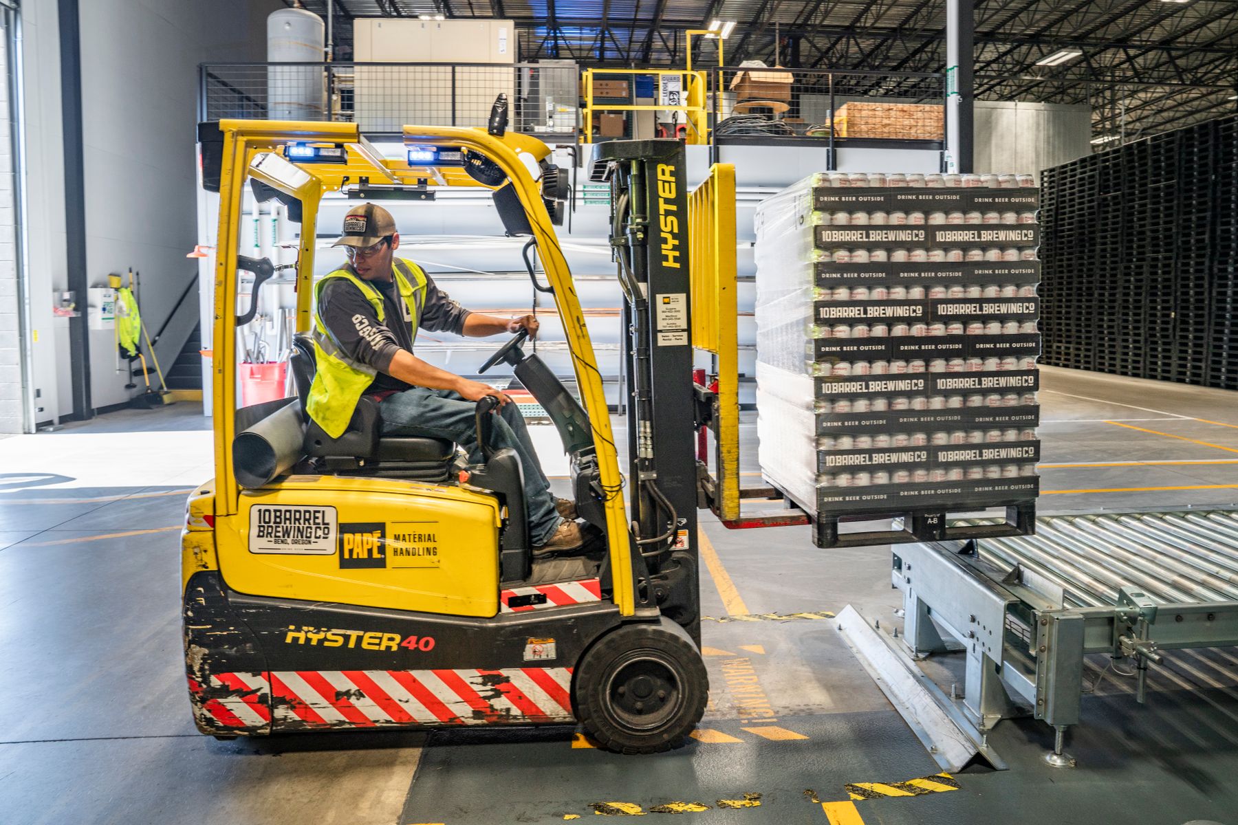 Forklift operator moving stacked pallets inside a distribution warehouse
